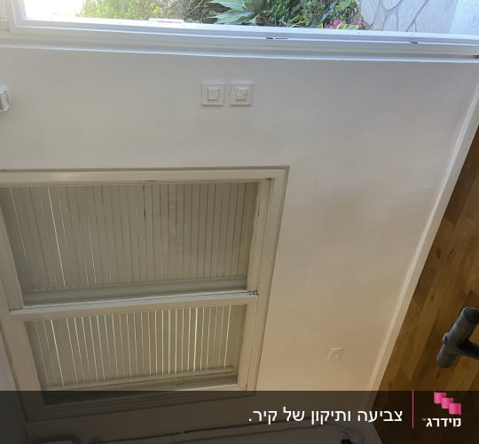 קיר פנימי צבוע מחדש בדירת מגורים לצד חלון ויציאה לחצר